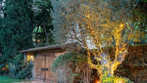 A rustic building with wooden doors and a tiled roof, surrounded by lush greenery and a well-maintained garden.