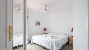 A bedroom with two beds, a ceiling fan, a nightstand, a lamp, and a painting on the wall. - Apartment 'Casa Sydhavshytten' with Sea View, Wi-Fi and Air Conditioning (Nerja)