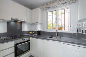 Una cocina moderna con armarios blancos, una campana extractora de acero inoxidable, un lavavajillas Bosch y una ventana con vistas a zonas verdes.