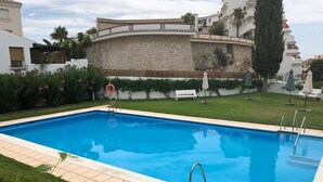 A rectangular swimming pool with a stone wall and a white building in the background. - Holiday Apartment "Casa Chana" with Terrace, Shared Pool and Jacuzzi (Almunecar)