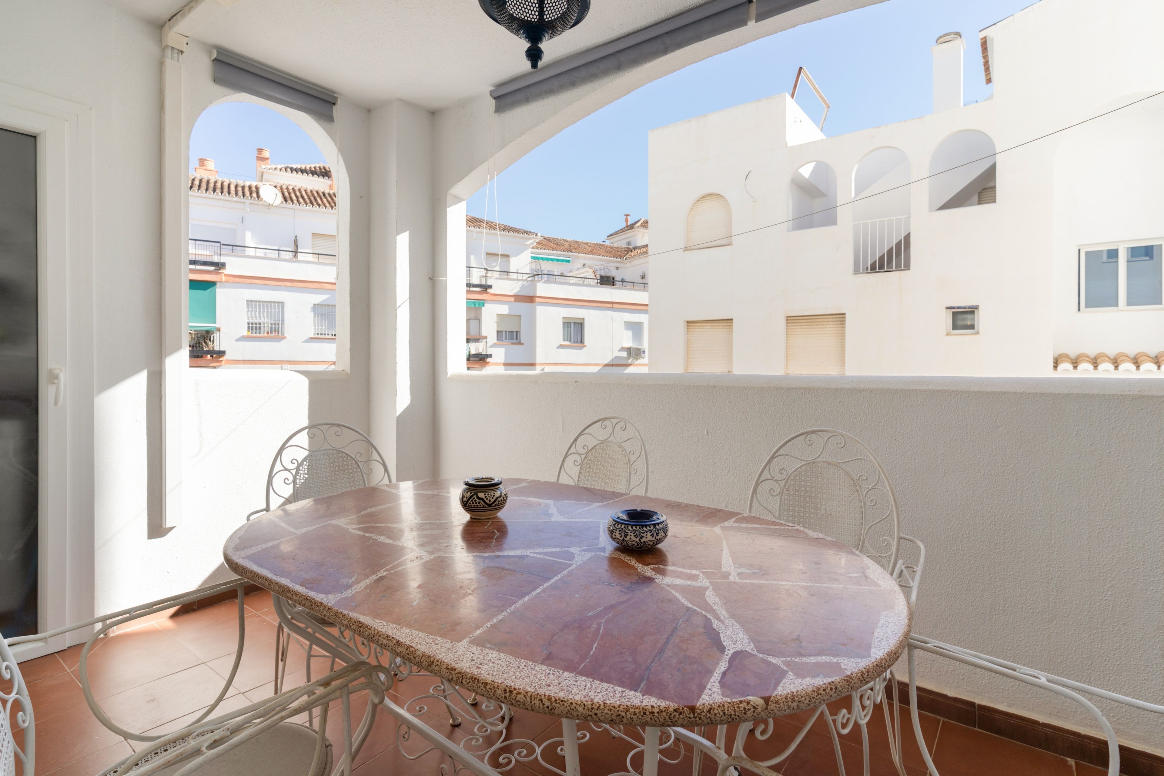 A round table with chairs in a balcony area, overlooking a residential neighborhood.