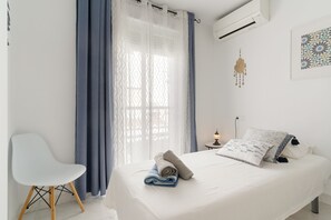 A modern bedroom with a bed, a chair, a bedside table with a lamp, and a wall-mounted air conditioner. - Holiday Apartment "Casa Chana" with Terrace, Shared Pool and Jacuzzi (Almunecar)