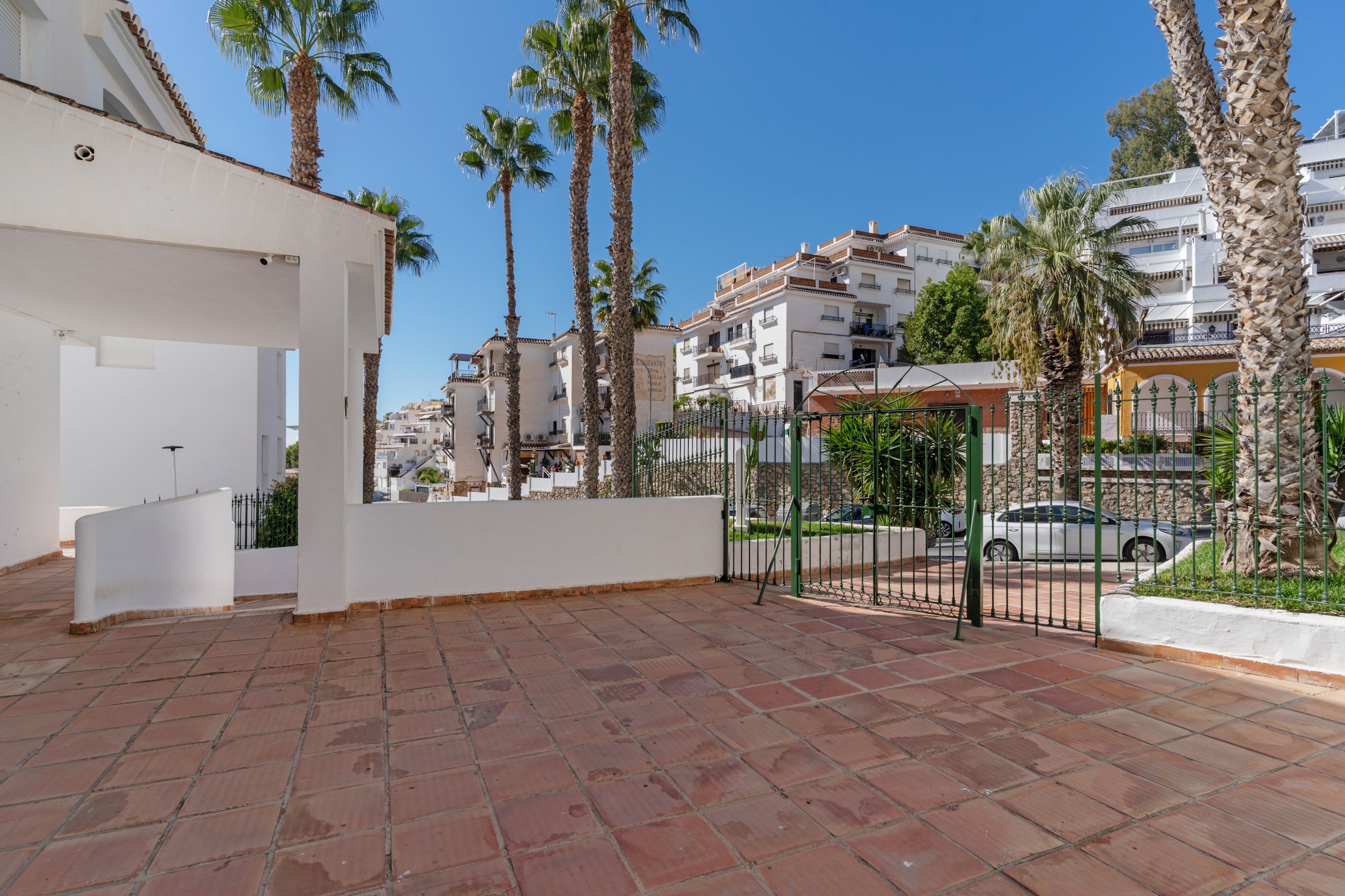 Un patio con tejas rojas, palmeras y un edificio blanco con balcones.