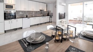 A modern kitchen with white cabinets, a built-in oven, and a dining area with a table set for two. - Holiday Apartment "Casa Chana" with Terrace, Shared Pool and Jacuzzi (Almunecar)