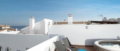 A rooftop terrace with a hot tub, lounge chairs, and a view of the sea.