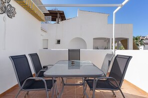 An outdoor patio with a table and chairs, a white wall, and a yellow-striped awning.