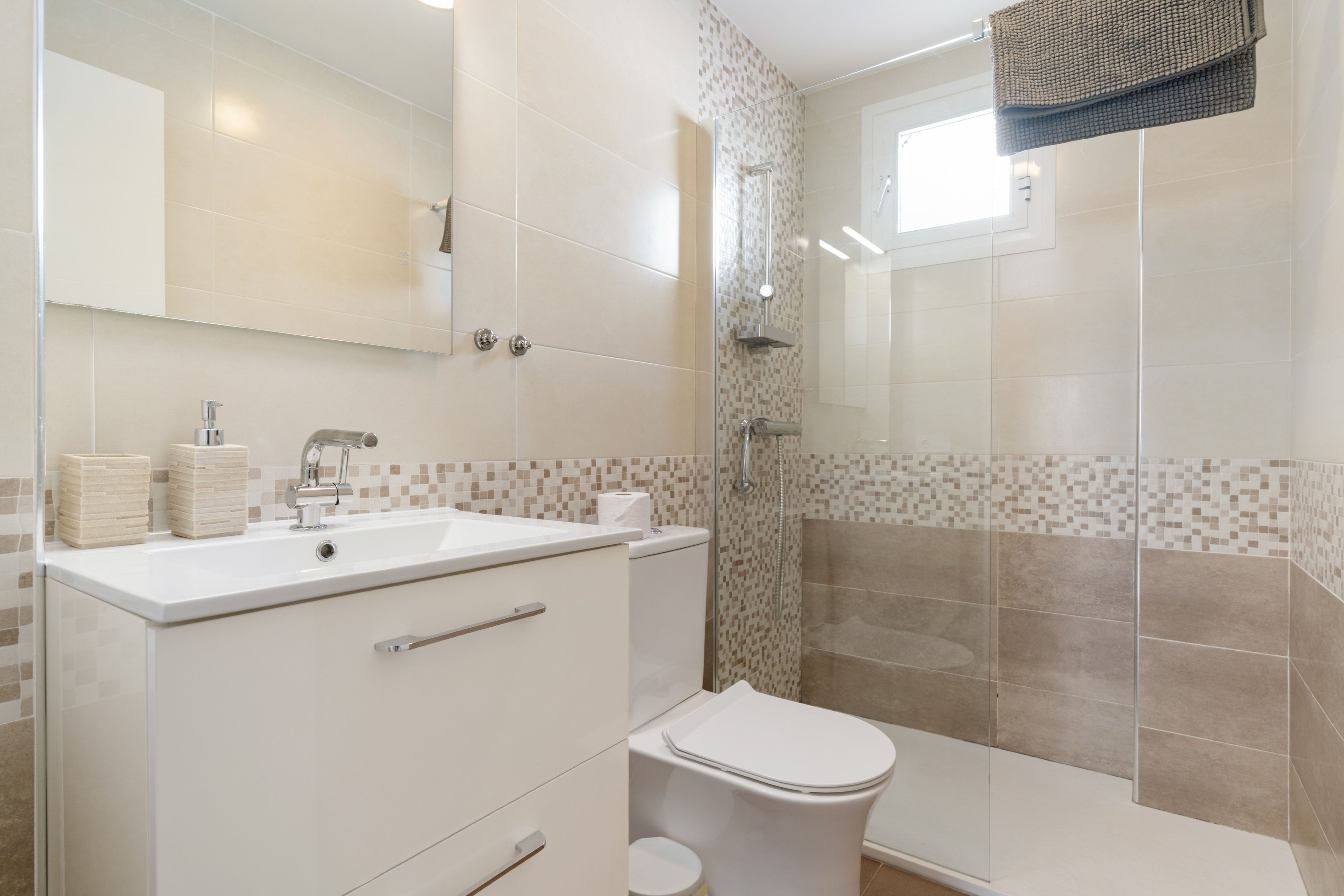 Un baño moderno con lavamanos, espejo y retrete blancos.