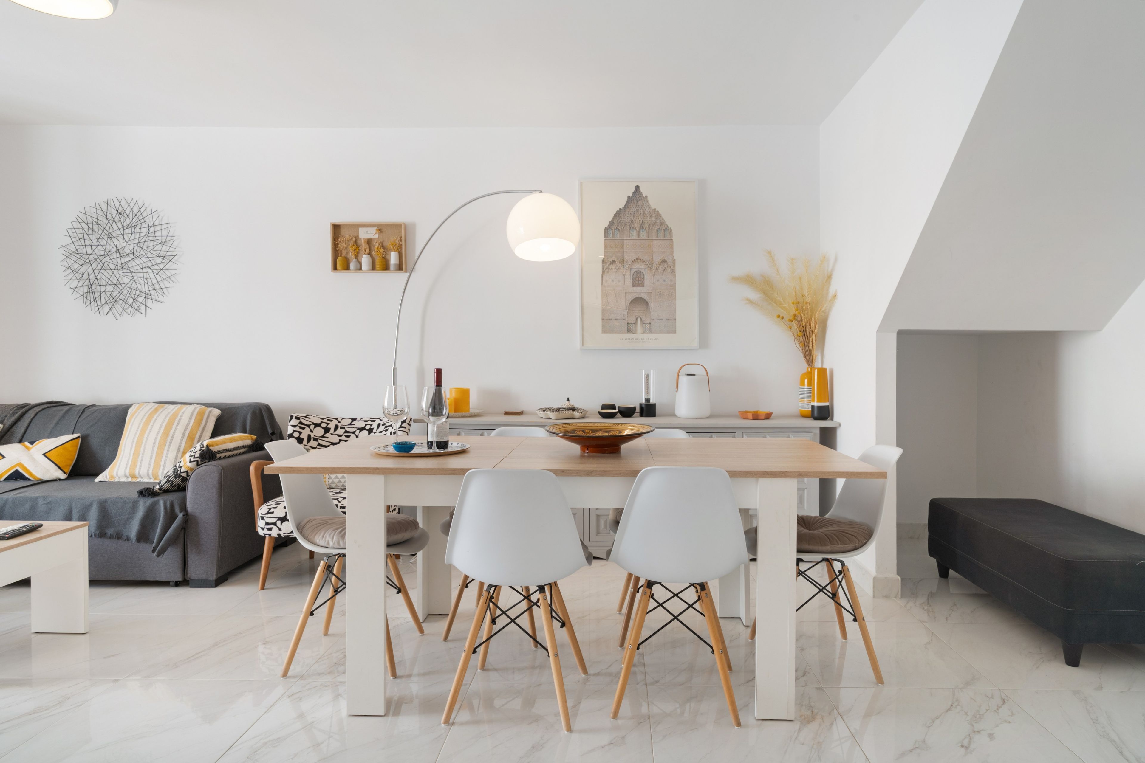 A modern living room with a dining area, featuring a sofa, a coffee table, a dining table with chairs, a floor lamp, and a fireplace.