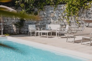 Une piscine bordée de chaises longues blanches et d’un mur en pierre.