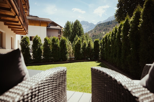 A patio with wicker chairs, a lawn, and a mountain view.
