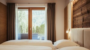 A hotel room with a bed, curtains, a wooden wall, and a view of trees through a glass door.