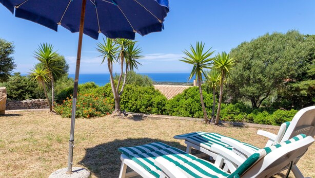 Eine Terrasse mit zwei gestreiften Liegestühlen, einem blauen Sonnenschirm und Blick aufs Meer.