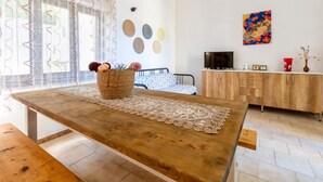 Ein Zimmer mit Holztisch, einem Korbwannenkorb, einer Spitzendecke, einem Bett mit gemustertem Kopfteil, einem Fernseher, einem Schrank und Wanddekoration.