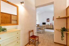 A hallway with a wooden chair, a wooden dresser, and a mirror. There is a dining area in the background with a table and chairs.