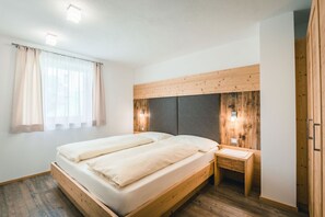 A double bed with a wooden headboard, a bedside table, and a window with curtains.