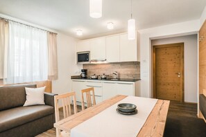 A compact living space with a kitchenette, a dining table, a sofa, and a wooden door.