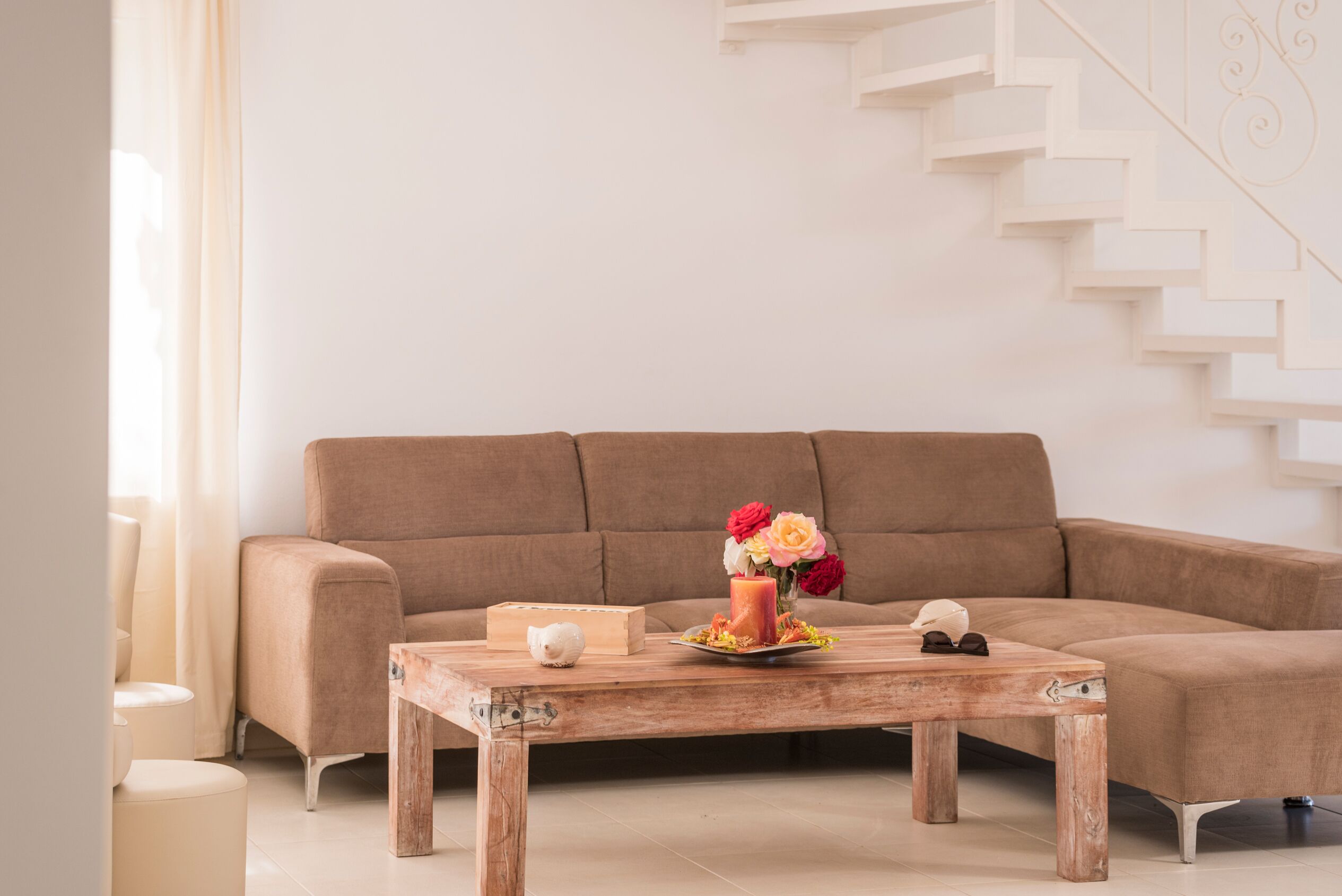 A living room with a brown sofa, a wooden coffee table with a candle, flowers, and a small white figurine.