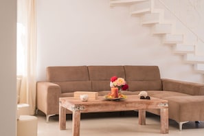 A living room with a brown sofa, a wooden coffee table with a candle, flowers, and a small white figurine.