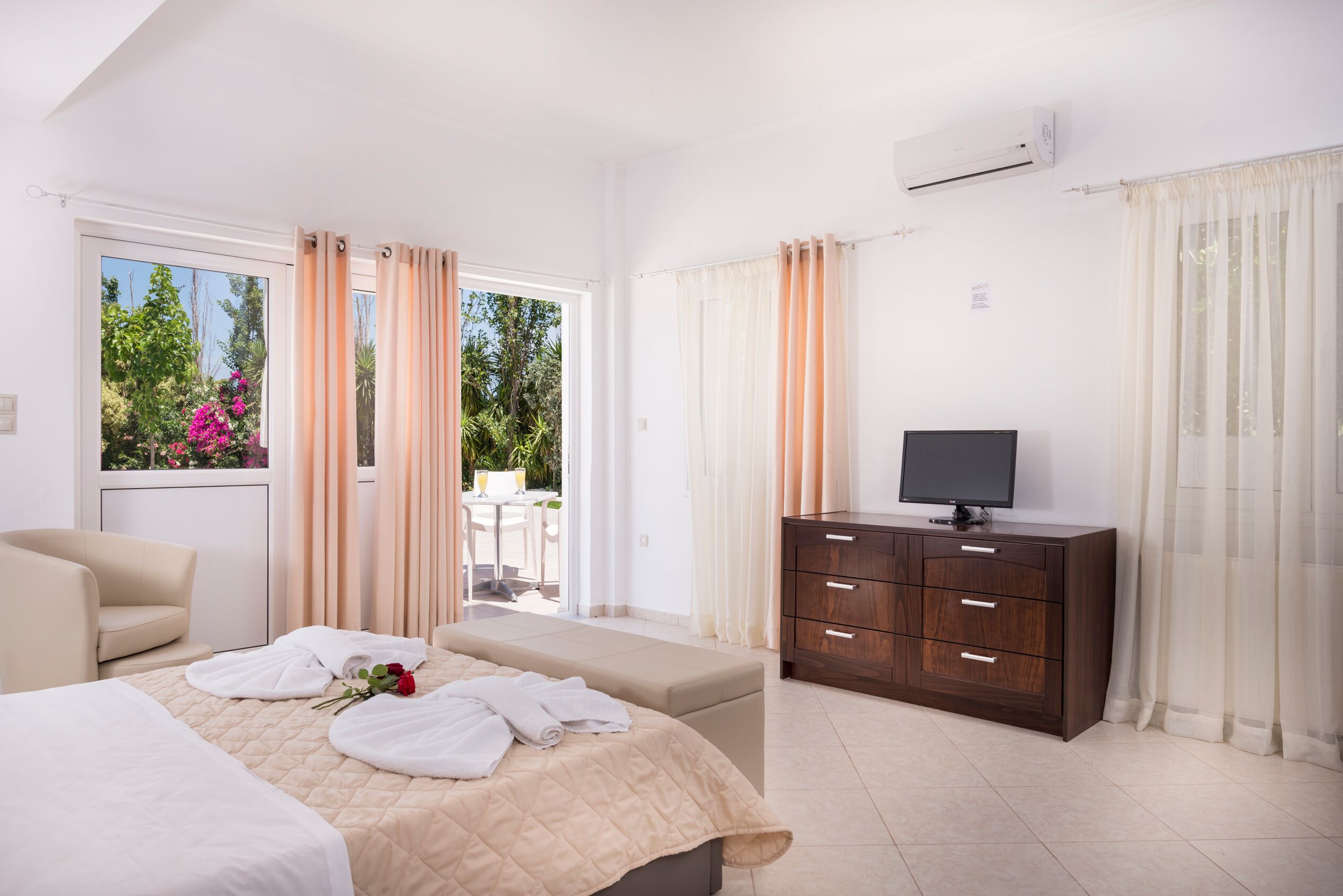 A hotel room with a bed, a TV, a dresser, and a balcony with curtains.