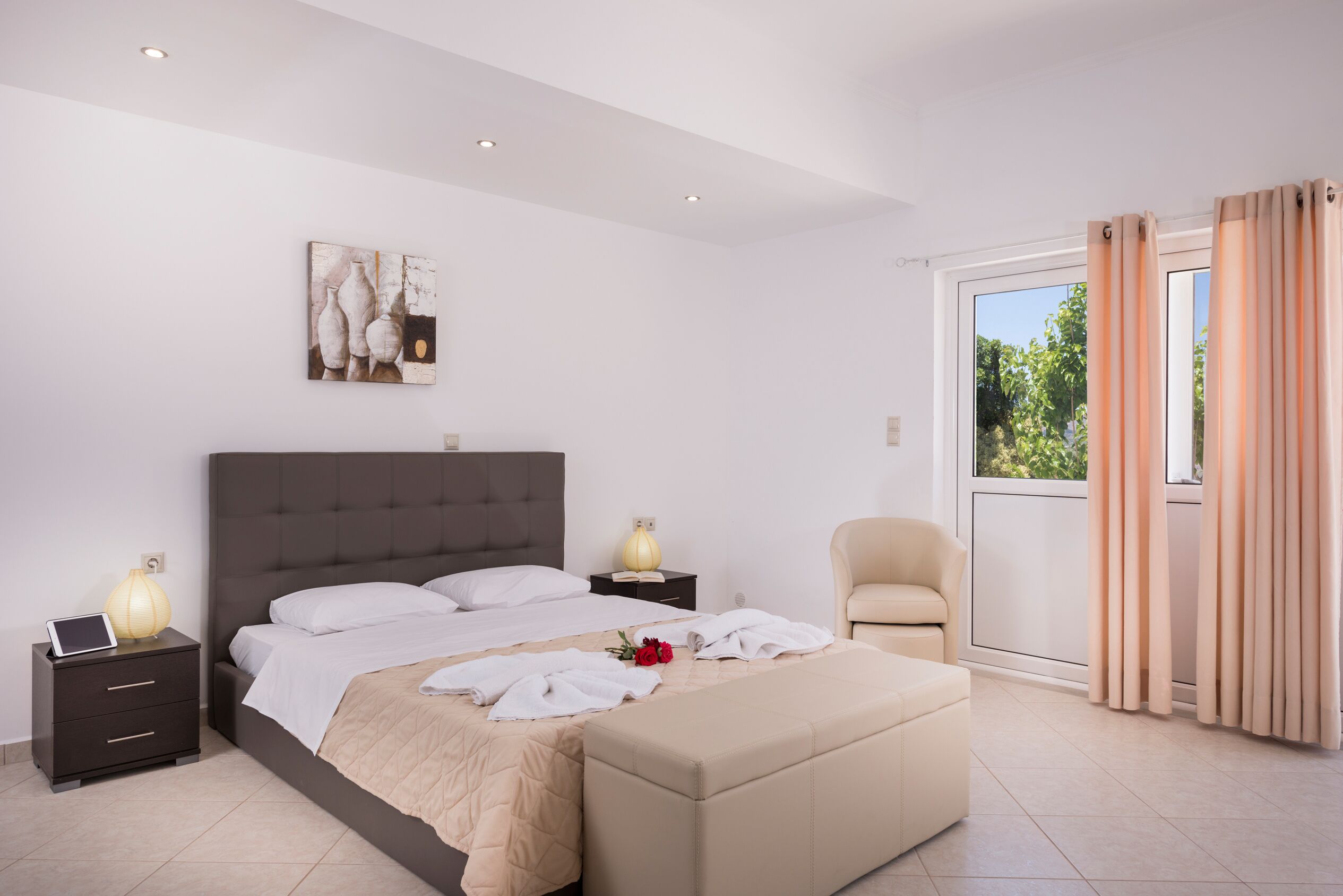 A modern bedroom with a large bed, bedside tables, a chair, and a window with curtains.