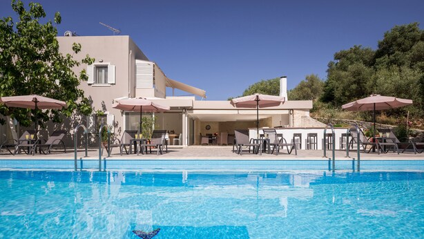 A swimming pool with a dolphin mosaic, lounge chairs, umbrellas, and a building with a terrace.