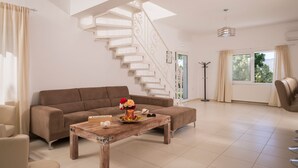 A spacious living room with a brown sofa, a wooden coffee table, and a white staircase.