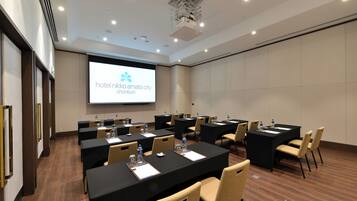 A conference room with multiple tables, chairs, and a projector screen displaying the hotel name.