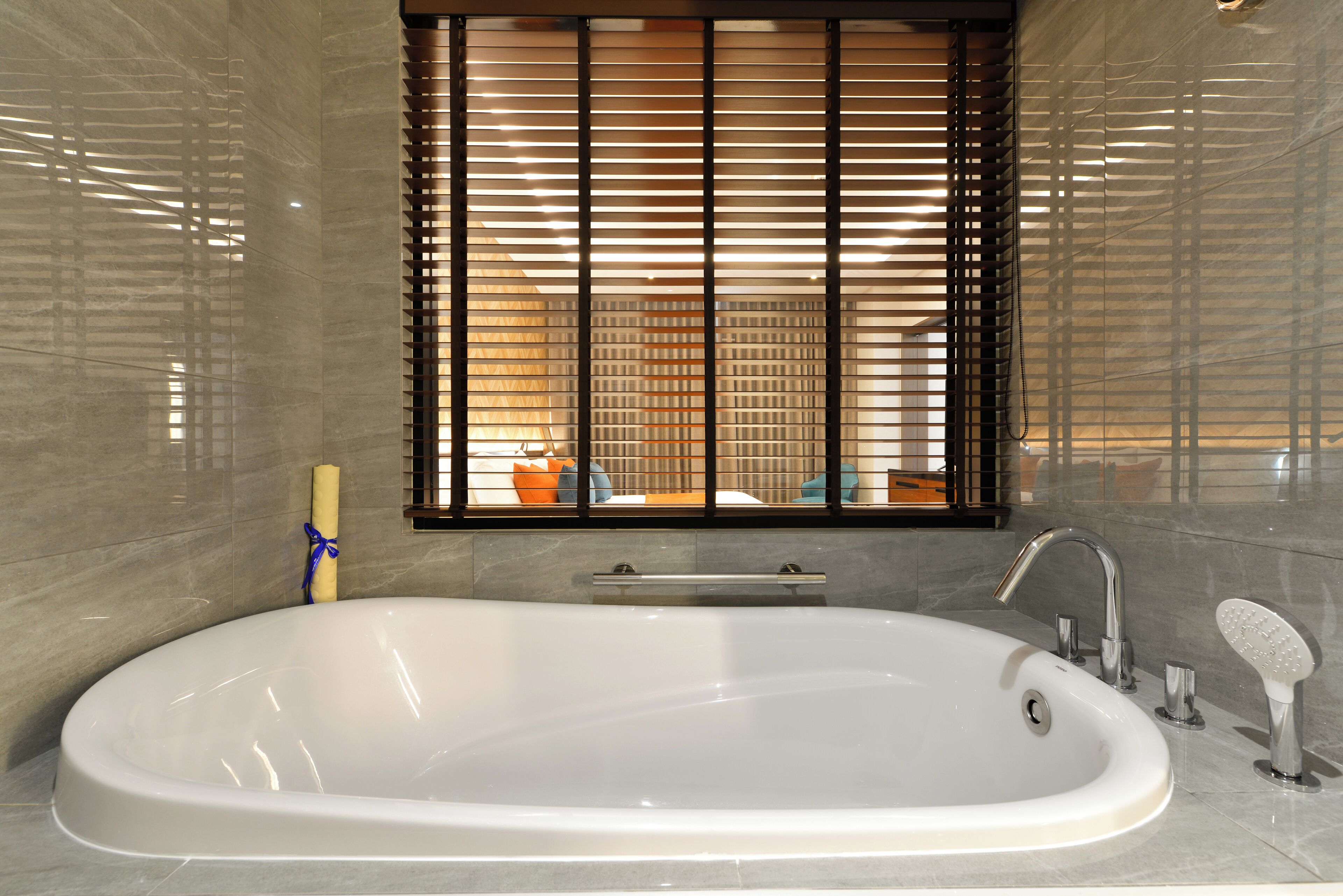 A modern bathroom with a large bathtub, a window with blinds, and a towel rack.