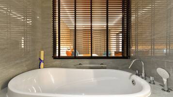 A modern bathroom with a large bathtub, a window with blinds, and a towel rack.
