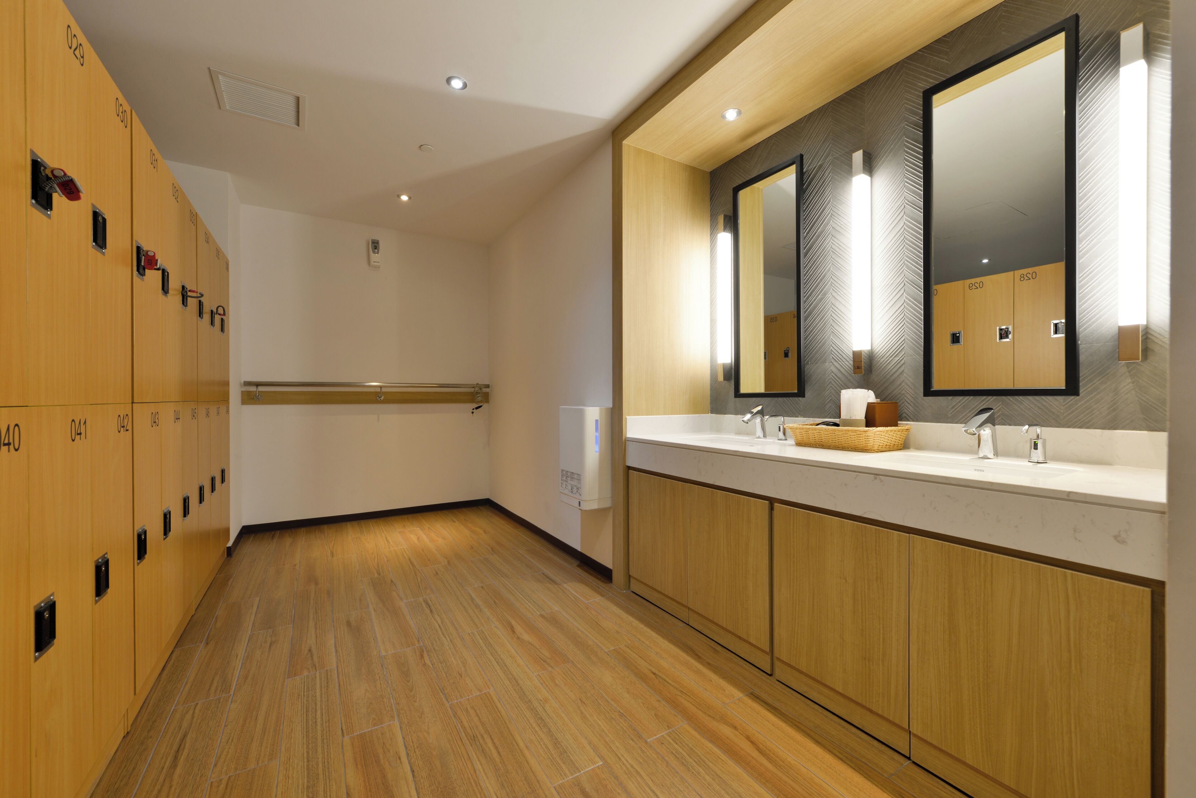 Un baño moderno con taquillas de madera, un lavamanos con espejo y un secador de manos.
