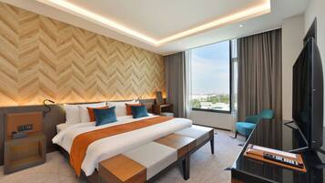 A modern hotel room with a large bed, a desk with a TV, and a city view through the window.