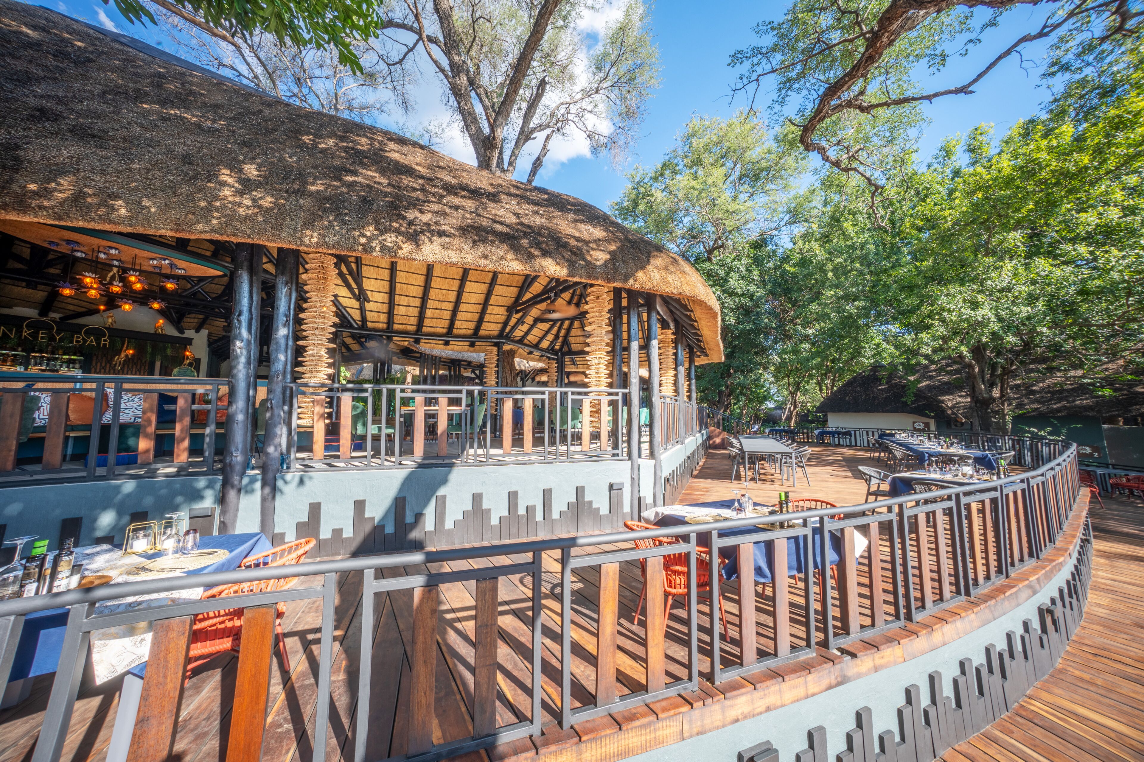 Un restaurant doté d’un toit de chaume, de tables en plein air et d’une terrasse en bois.