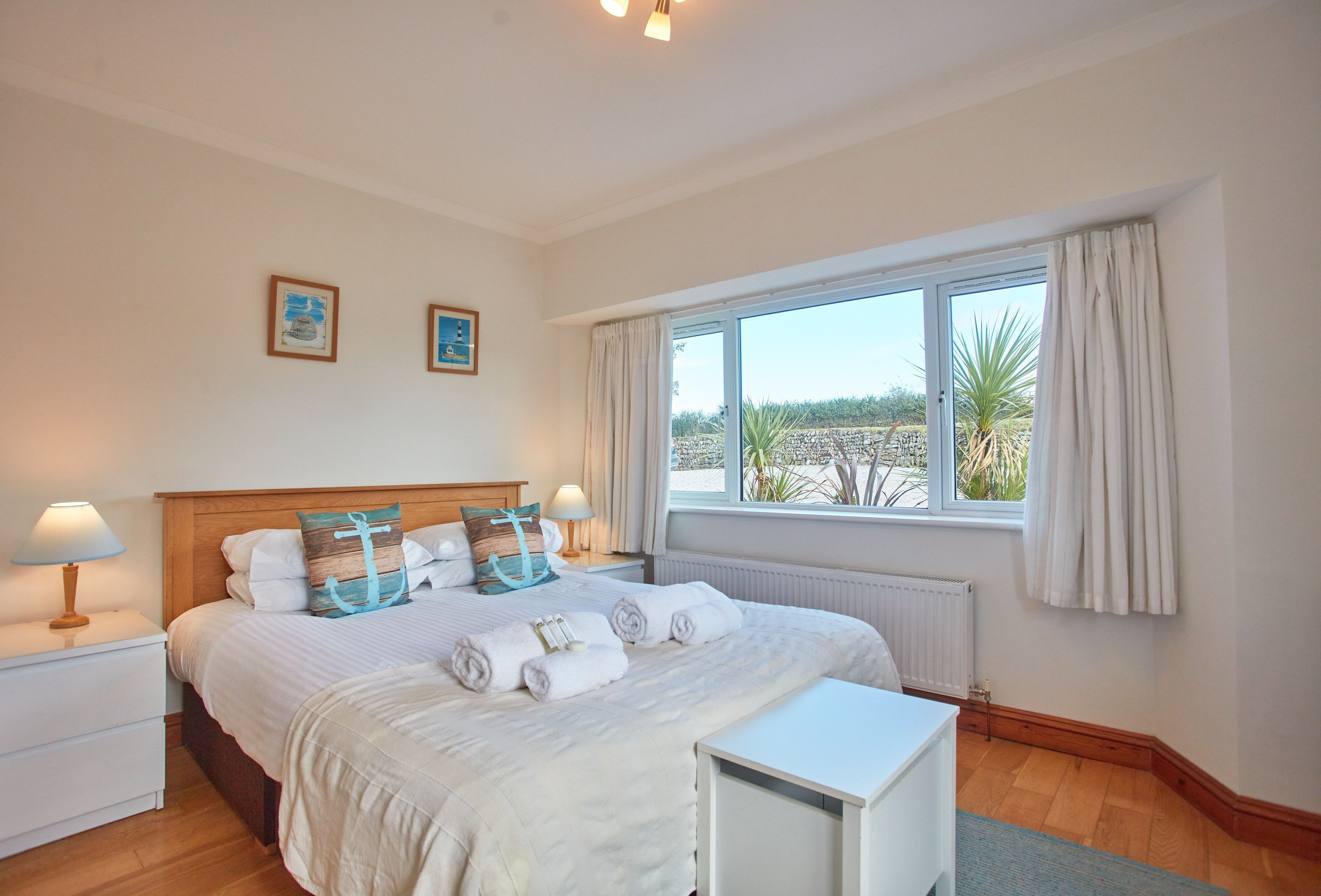A hotel room with a large bed, two bedside tables with lamps, a window with curtains, and artwork on the wall.