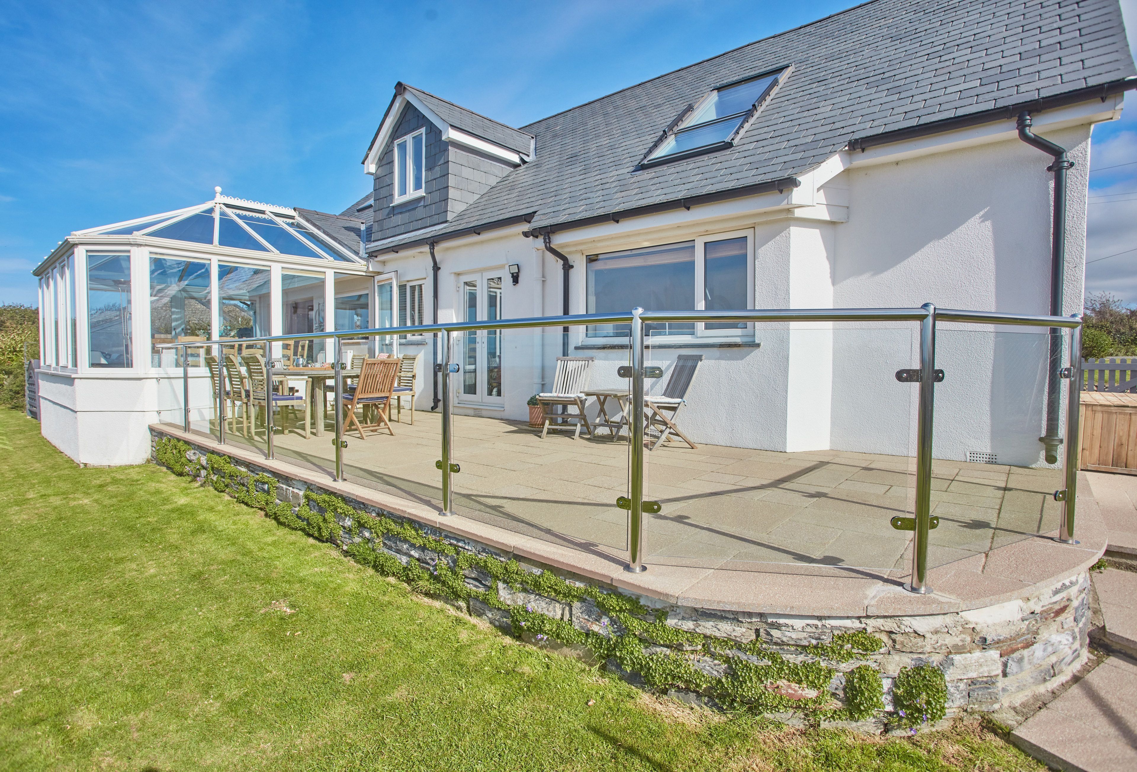 A house with a conservatory, a patio with outdoor furniture, and a stone retaining wall.