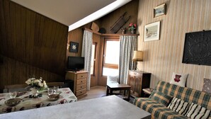 Una sala de estar acogedora con pared de madera, televisor, sofá escocés y una mesa de comedor decorada con flores.