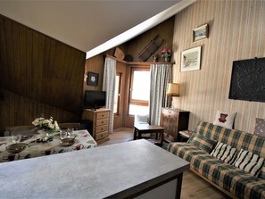 Uma sala de estar aconchegante com uma parede de madeira, uma televisão, um sofá xadrez e uma mesa de jantar decorada com flores.