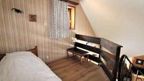 Un dormitorio con cama de madera, un banco, una escalera y una ventana con cortinas.