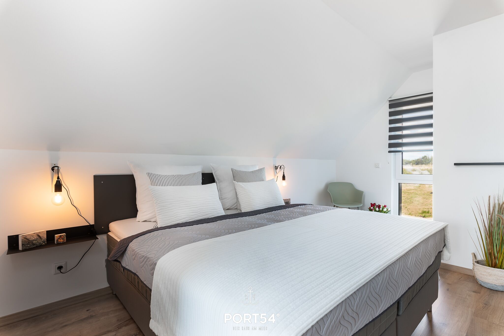 A modern bedroom with a large bed, bedside tables, and a window with blinds.