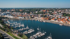 En småbåtshamn med många förtöjda båtar, omgiven av en stad med historiska byggnader och en klar himmel.