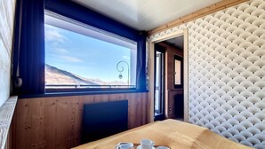 Une pièce avec une grande fenêtre, un lit, une table avec un plateau, et un mur orné d’un motif.