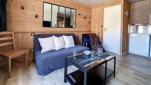 L’intérieur d’une cabane en rondins moderne, avec un canapé, deux fauteuils, une table basse en verre et un coin cuisine.