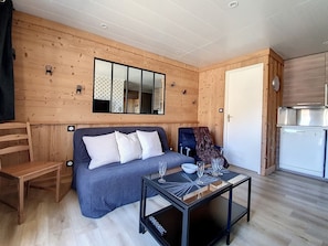 A modern log cabin interior with a sofa, two armchairs, a glass-top coffee table, and a kitchen area. - Charming Renovated 2-Room, Near Slopes, Balcony, Outdoor Parking (Saint-Martin-de-Belleville)