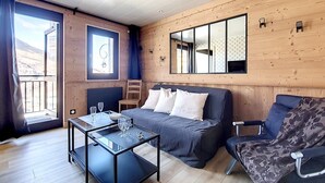 Une pièce moderne avec un plancher en bois, un canapé, un fauteuil, une table basse en verre et une grande fenêtre.