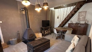 A living room with a sofa, a wooden chest, a fireplace, a dining table, and a staircase.