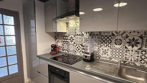 A modern kitchen with a black and white patterned backsplash, a coffee maker, a blender, and a stainless steel sink.