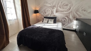 A bedroom with a bed, a wall mural of white roses, a lamp, and a wardrobe.