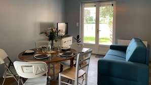 A dining area with a table set for four, a blue sofa, and a television on a cabinet. - Renovated cottage in Pierrefitte-sur-Loire with garden and parking (Pierrefitte-sur-Loire)
