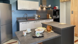 A modern kitchen with a built-in oven, a microwave, and a sink. There is a wooden cabinet and a countertop with various kitchen items. - Renovated cottage in Pierrefitte-sur-Loire with garden and parking (Pierrefitte-sur-Loire)