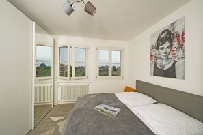 A bedroom with a bed, a window, a radiator, and a painting on the wall. - Corte Fasanella 31 - Gardagate (Toscolano-Maderno)