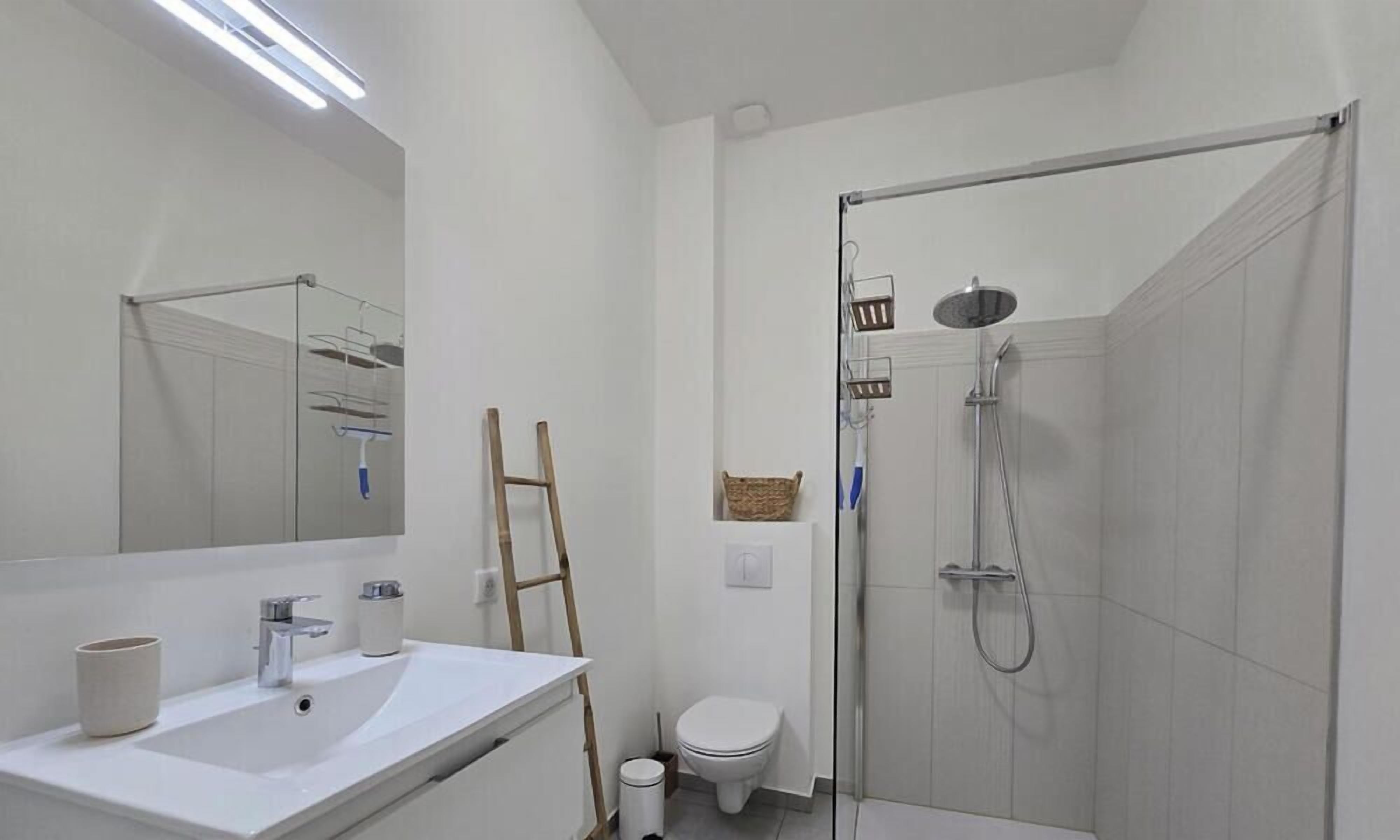 A modern bathroom with a white sink, mirror, toilet, and glass-enclosed shower.
